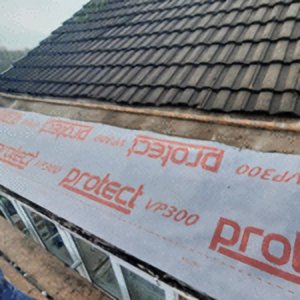 A close-up shot of a roofing project showing the installation of a Protect VP300 breathable underlay membrane beneath dark roof tiles